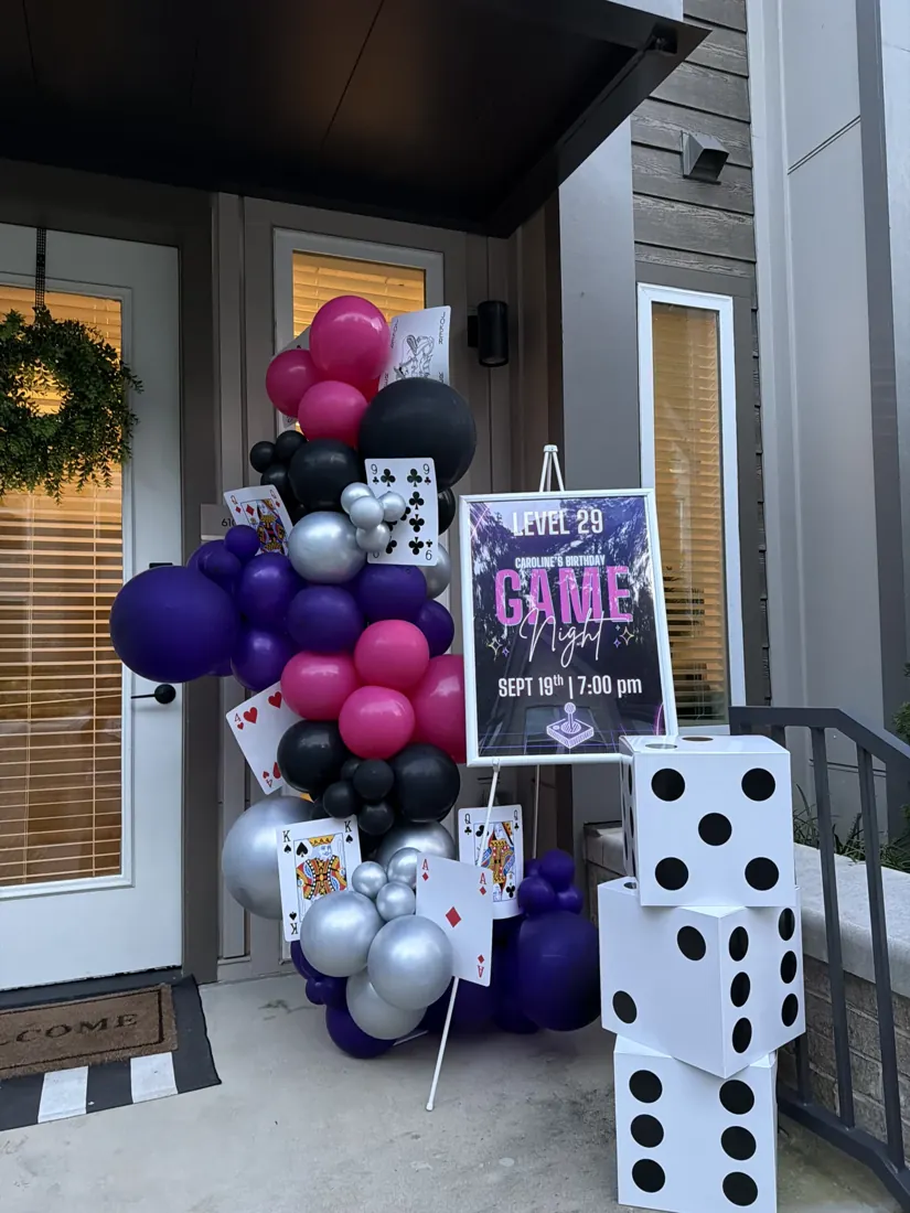 Purple, pink, black and silver balloons with oversized dice at a game night display